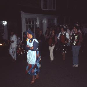 People in costume playing instruments walking along road at night