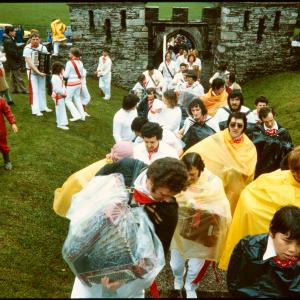 Old Oss procession accordion players wearing rain ponchos, walking through Prideaux Place gates