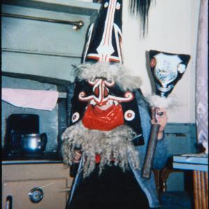 Woman wearing Blue Ribbon hat, holding club, in kitchen