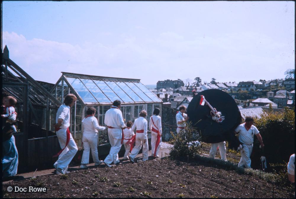 Old Oss, followed by procession, walking past greenhouse