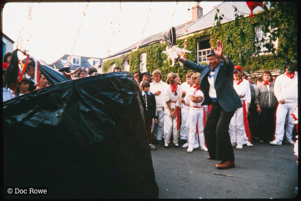 Man teasing Old Oss under maypole at sunset
