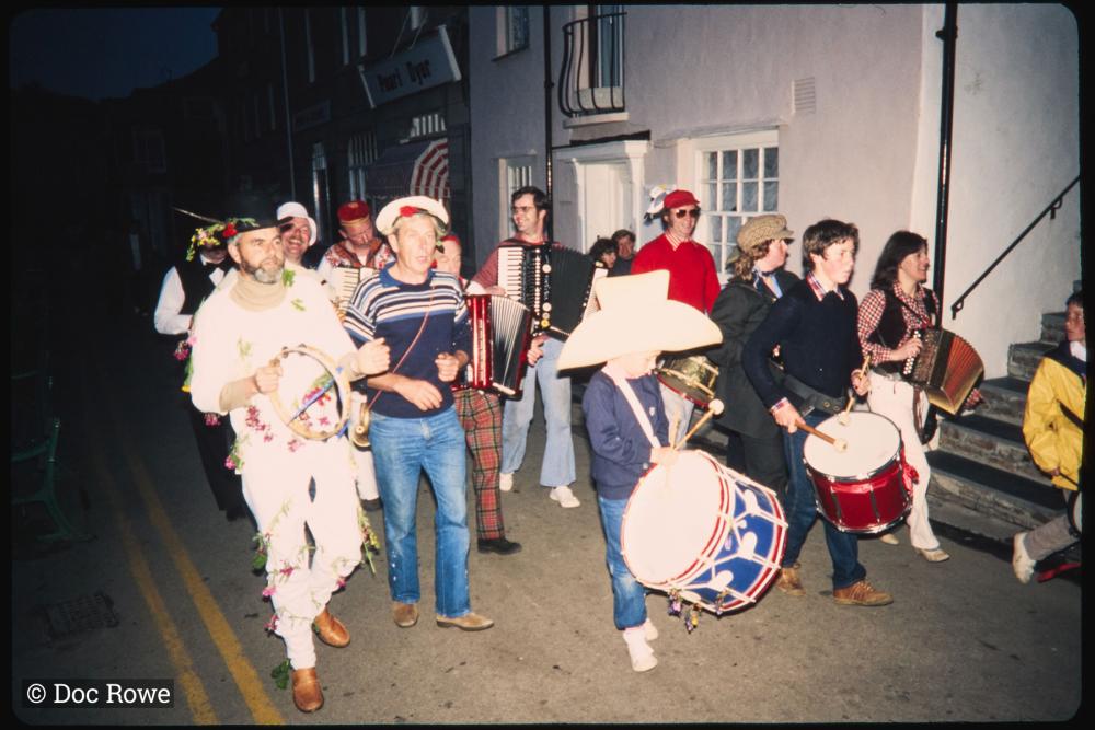 People in costume playing instruments walking along road at night