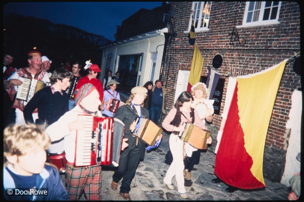 People in costume playing instruments walking along road at night