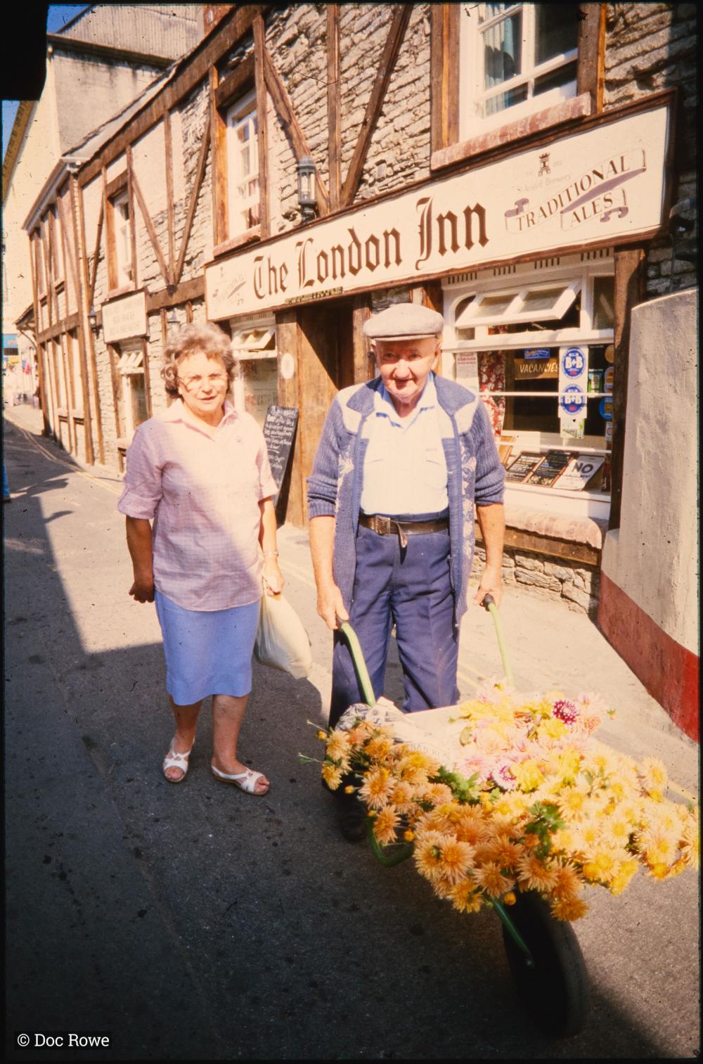 Man and woman with wheelbarrow full of flowers outside The London Inn