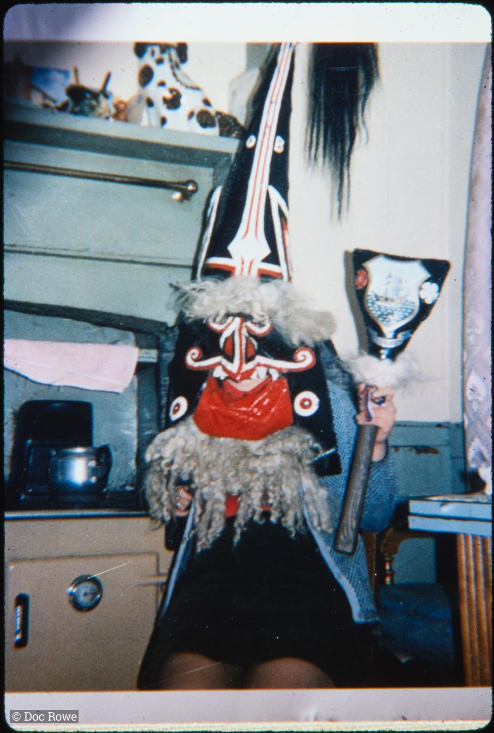 Woman wearing Blue Ribbon hat, holding club, in kitchen